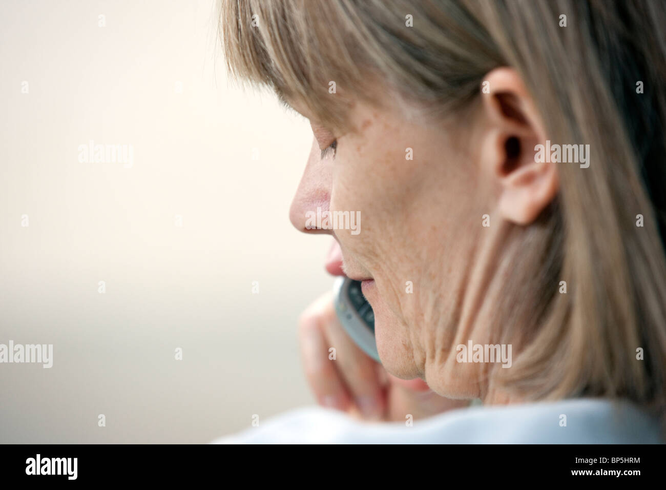 Close up of a middle aged woman talking on a telephone while seated outside in a residential yard. Stock Photo