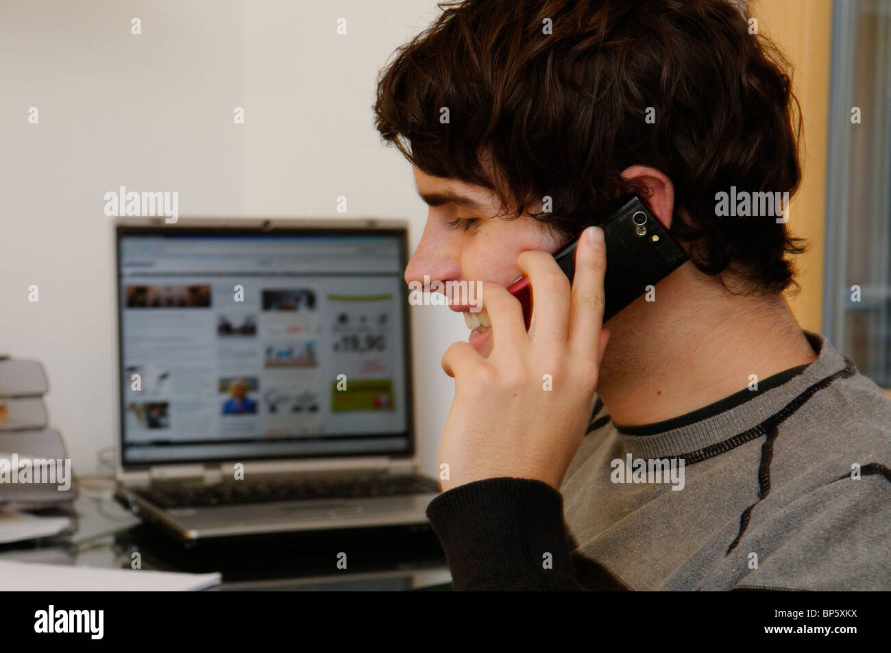 Notebook Open. Phone young man talking on mobile phone with laptop open in the background ...