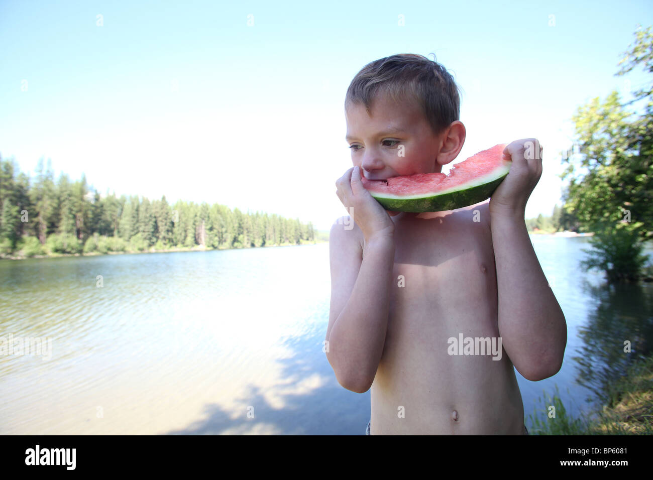 young boy eating a slice of watermelon by lake Stock Photo