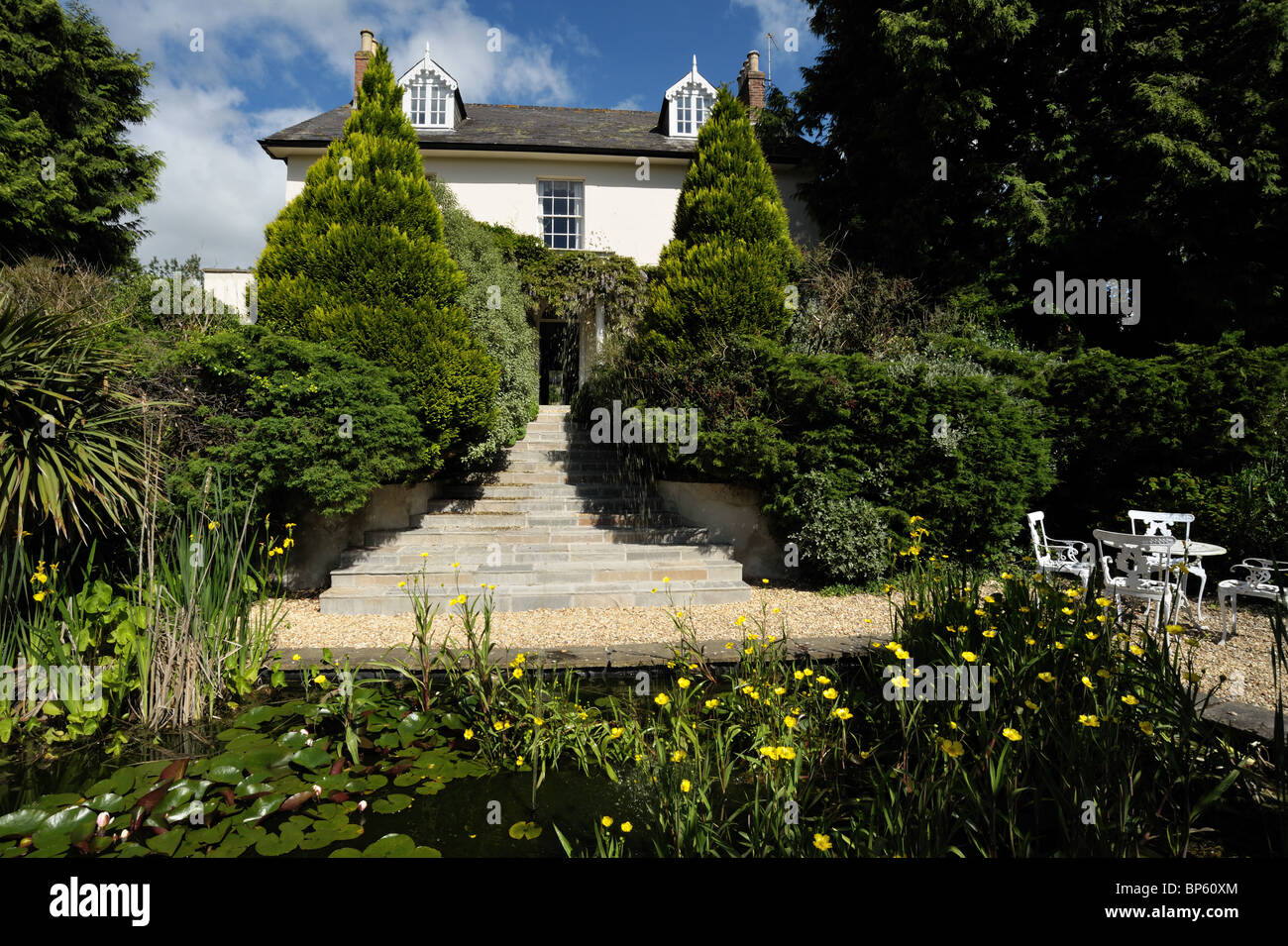 Mature garden with stone steps leading to a Georgian house, a pond in the foreground Stock Photo