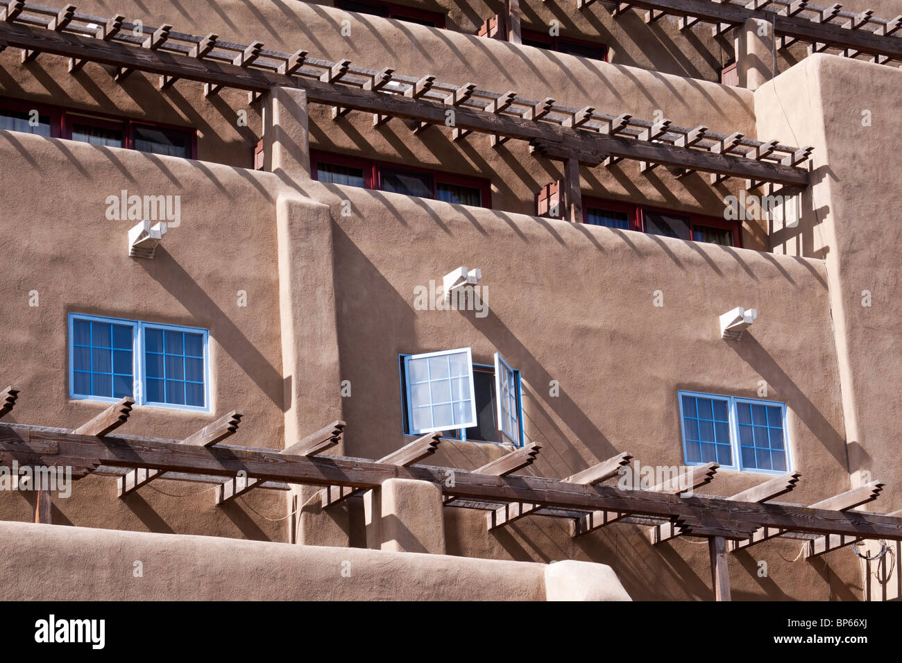 Three windows and many vigas casting shadows on a building in the Pueblo revival style architecture in Santa Fe, New Mexico Stock Photo