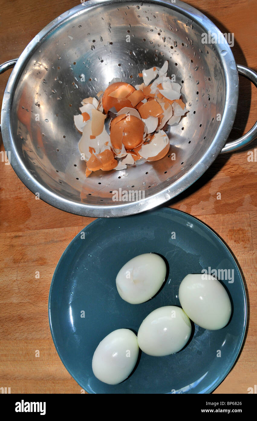 A plate of shelled boiled eggs next to a  sieve containing their shells. Stock Photo