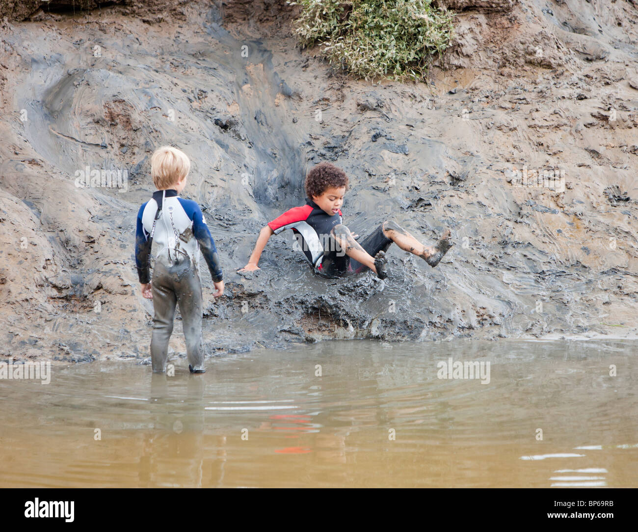 Boys playing in a muddy creek in Blakeney, Norfolk, UK. Stock Photo