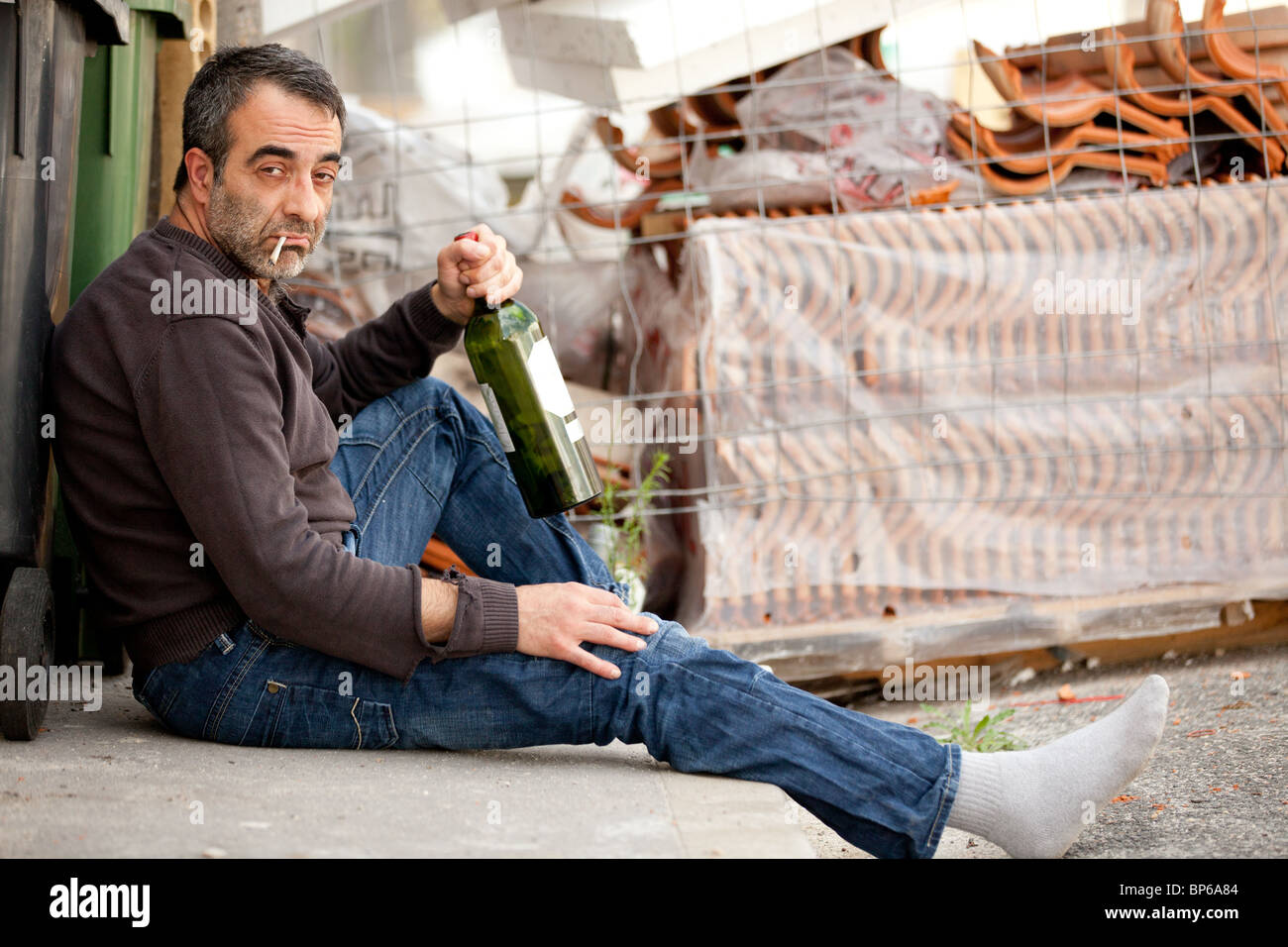 poor drunk man lying near trashcan in city street Stock Photo