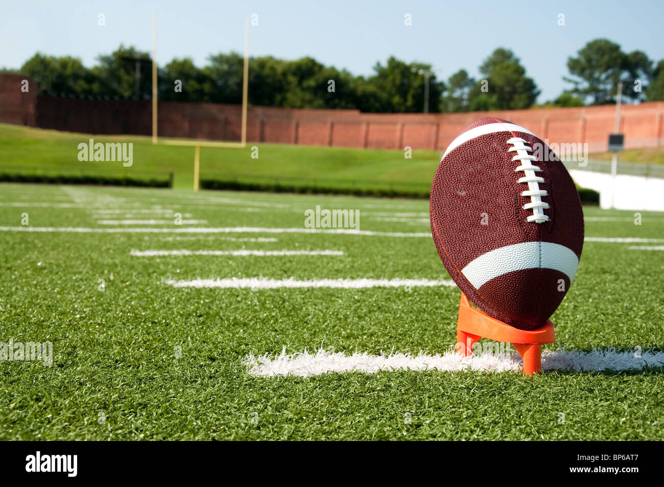 American football on kicking tee on field with goal post in background. Stock Photo