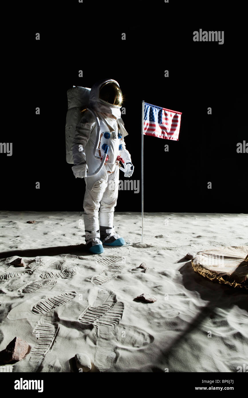 An astronaut on the moon standing next to an American flag Stock Photo
