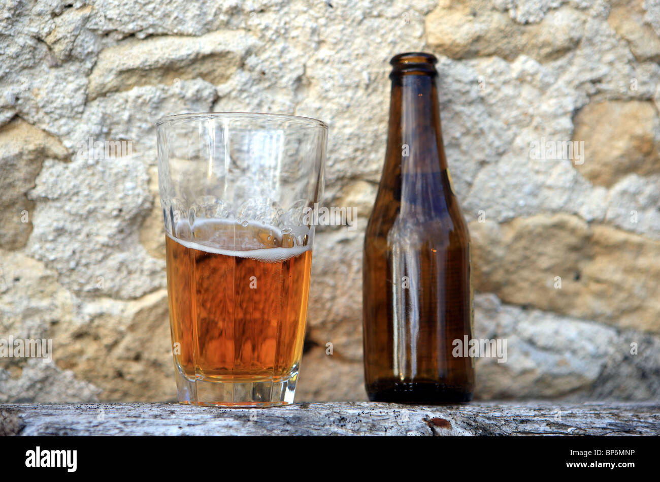A beer glass and bottle resting on old wood outside an old house on a summer evening Stock Photo