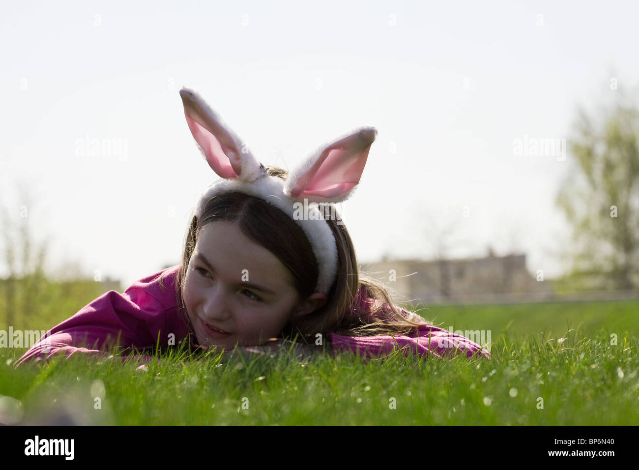 A girl wearing rabbit ears and lying down on grass Stock Photo