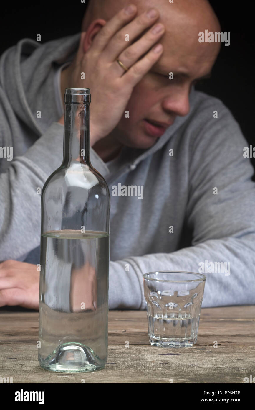 A drunk and depressed man with a bottle of vodka and an empty glass