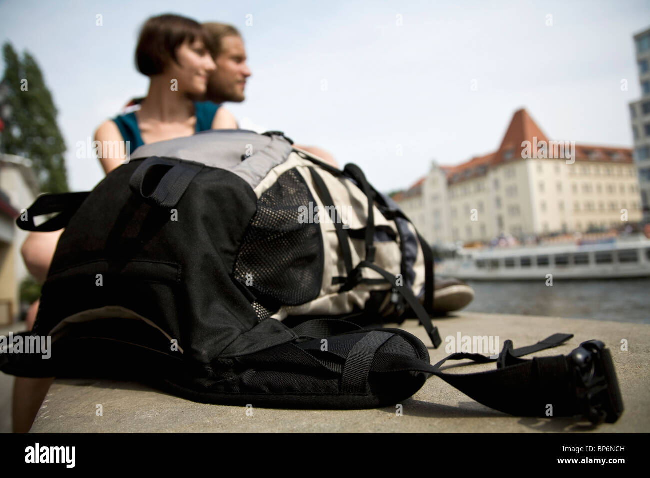 A backpack and a young couple by the Spree river, Berlin, Germany ...