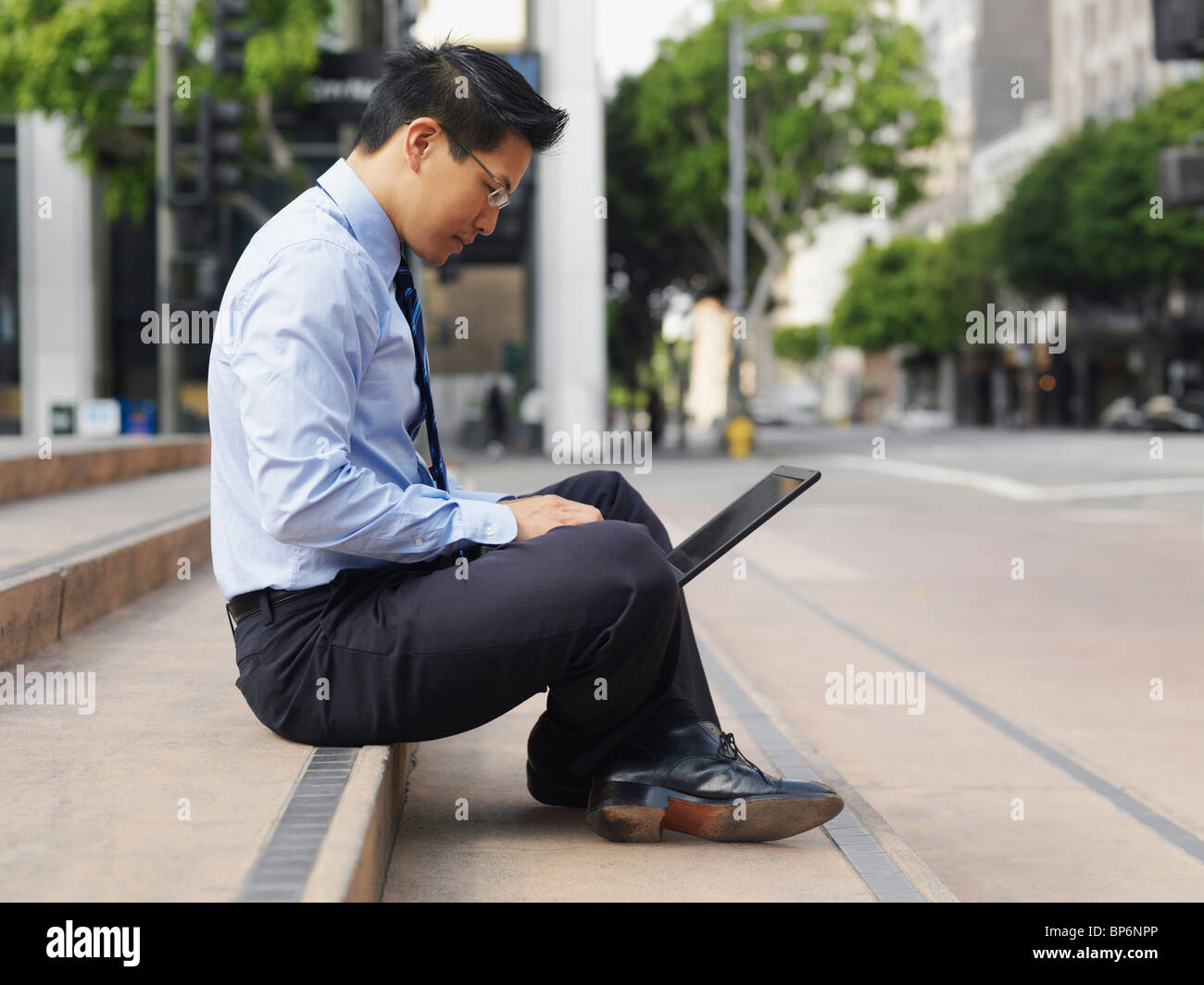 A businessman sitting cross-legged on some steps, using a laptop Stock Photo