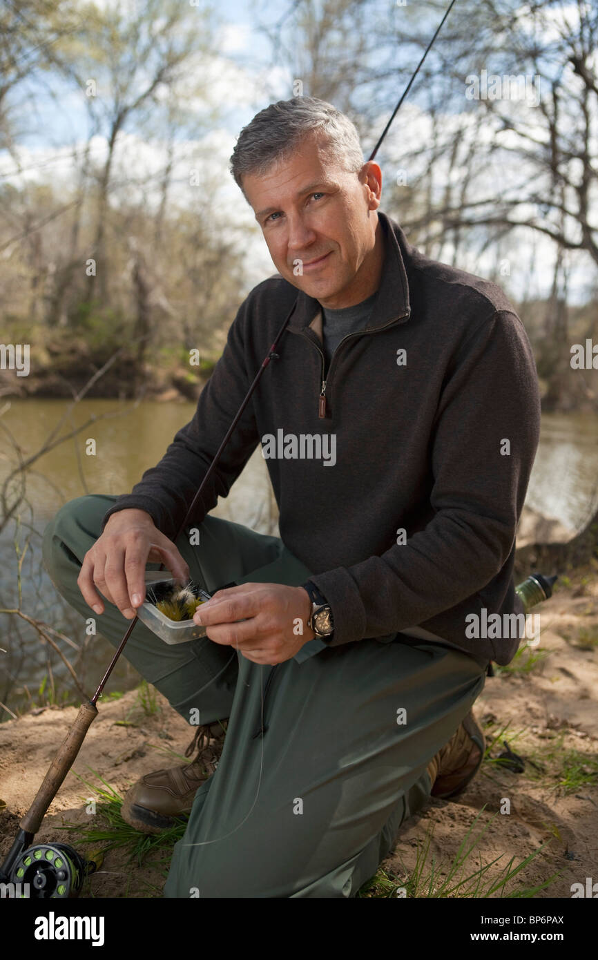 Portrait of a man kneeling next to a river with fishing equipment Stock Photo