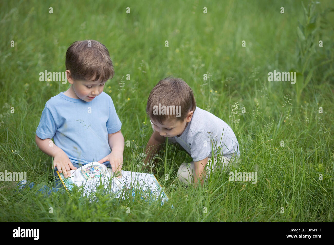 Two boys looking at a book in a field Stock Photo