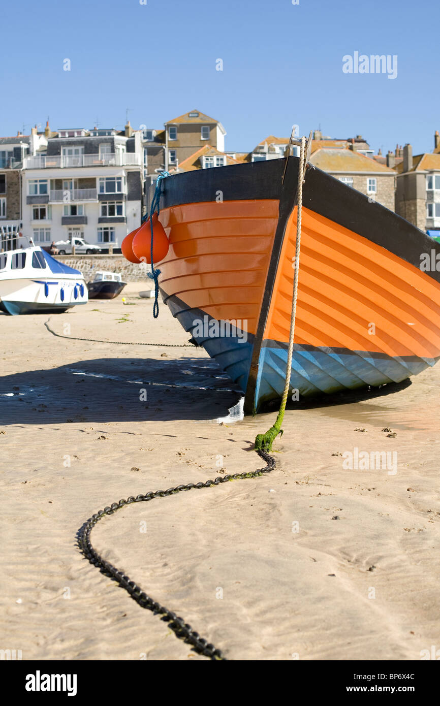 An orange hulled fishing boat on the sand at low tide in St Ives harbour. Stock Photo