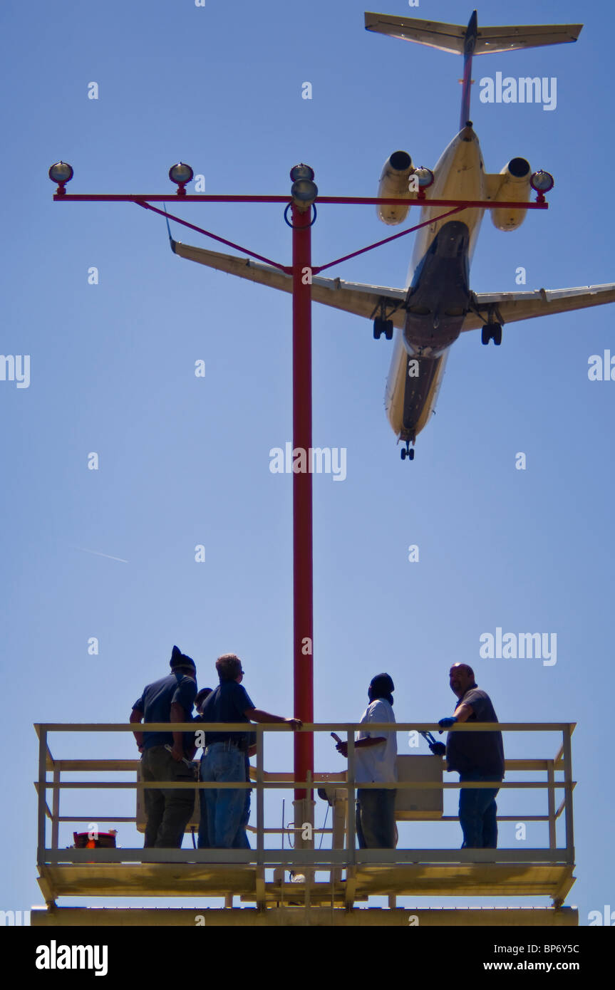 People working on runway approach lights beneath jet airplane landing at Los Angeles Int'l Airport LAX, California  Stock Photo