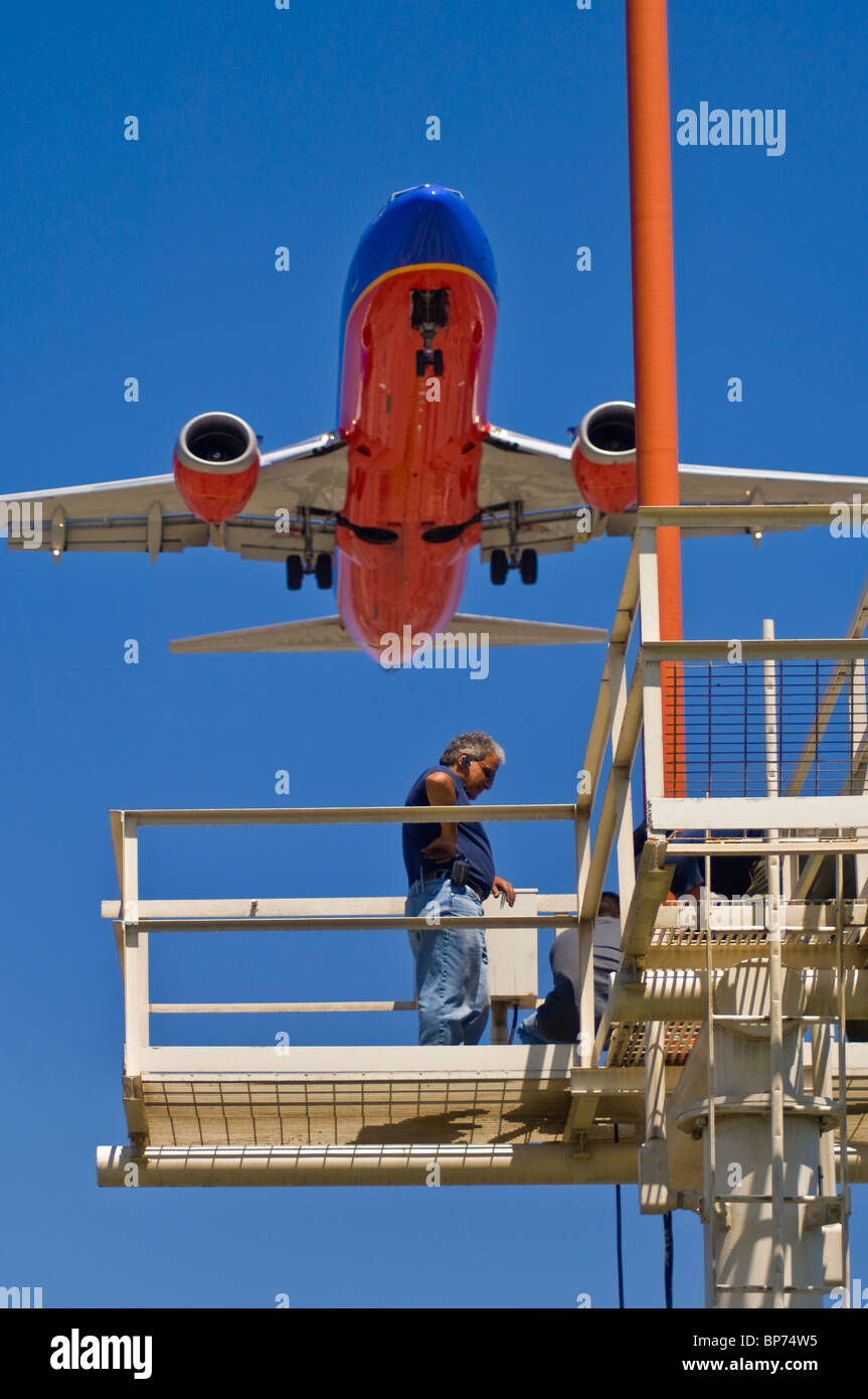 People working on runway approach lights beneath jet airplane landing at Los Angeles Int'l Airport LAX, California  Stock Photo