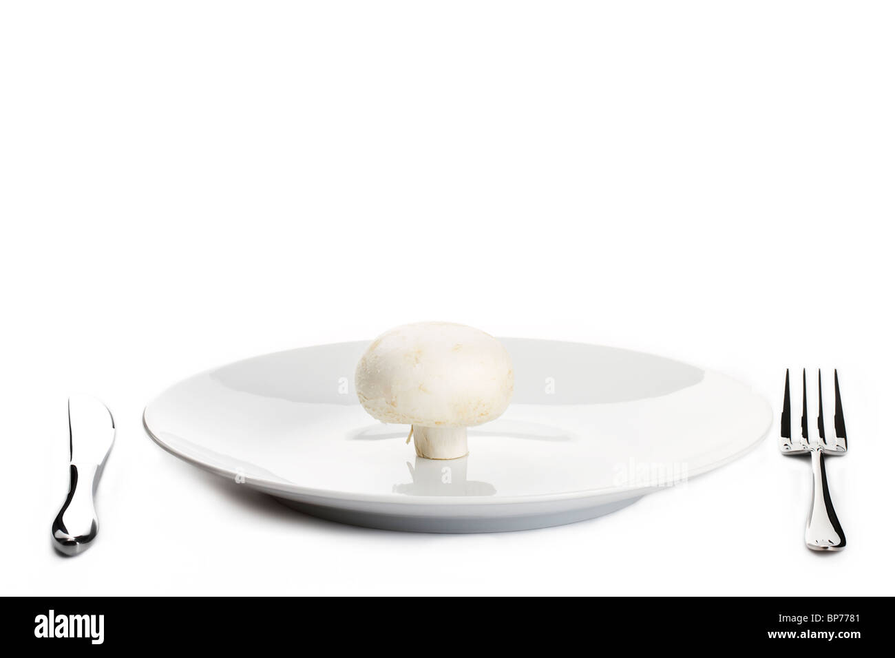 one white mushroom on a plate with knife and fork Stock Photo