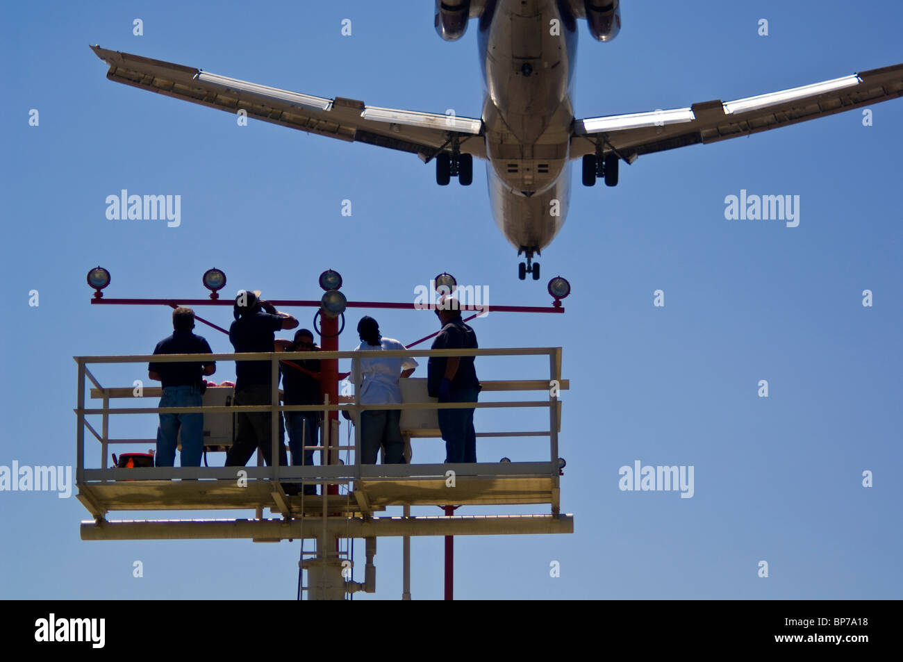 People working on runway approach lights beneath jet airplane landing at Los Angeles Int'l Airport LAX, California Stock Photo