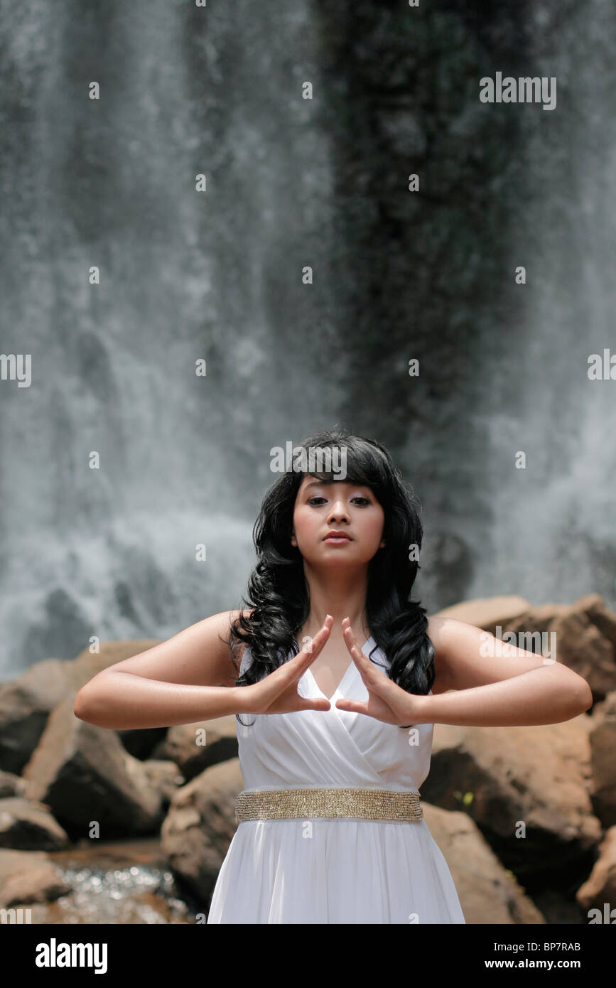 girl meditating and praying with waterfall in the background Stock Photo