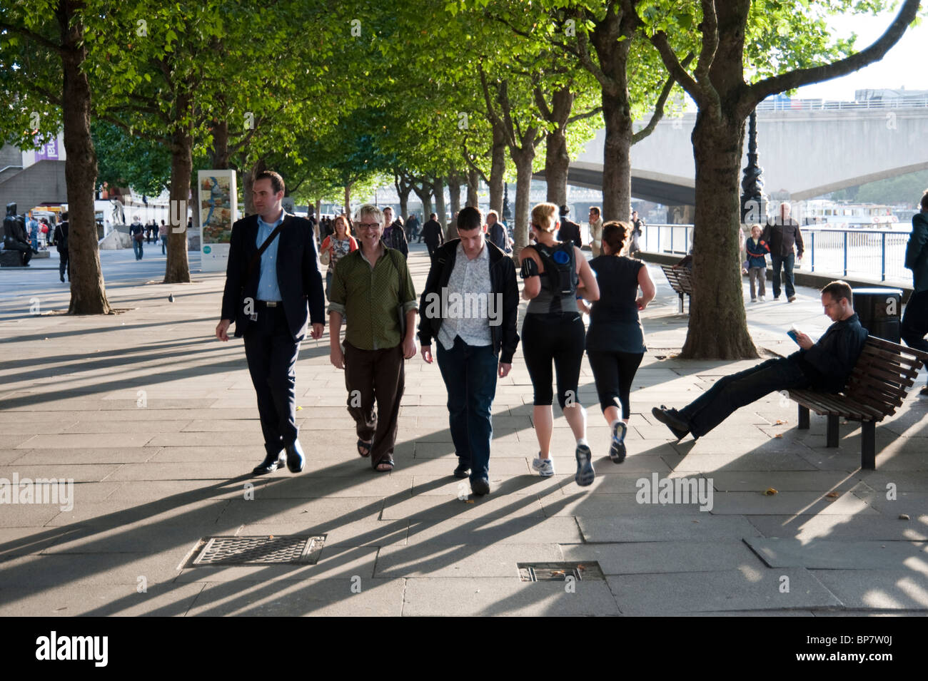Group of people walking in evening sunshine at the Southbank next to the River Thames, London, UK Stock Photo