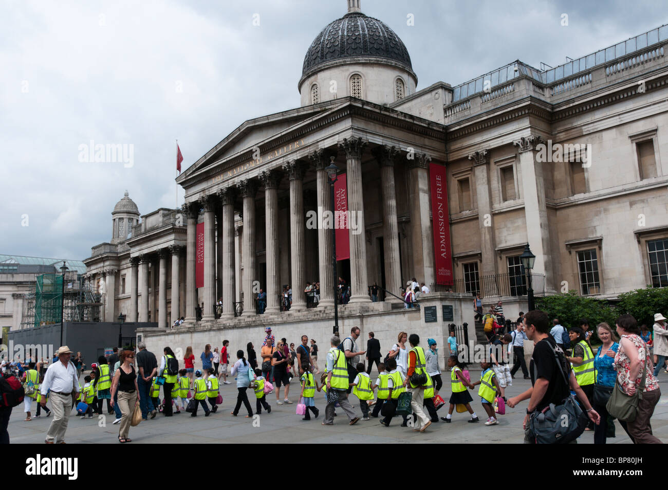 A group of school children on an outing cross Trafalgar Square in London wearing high-vis jackets Stock Photo