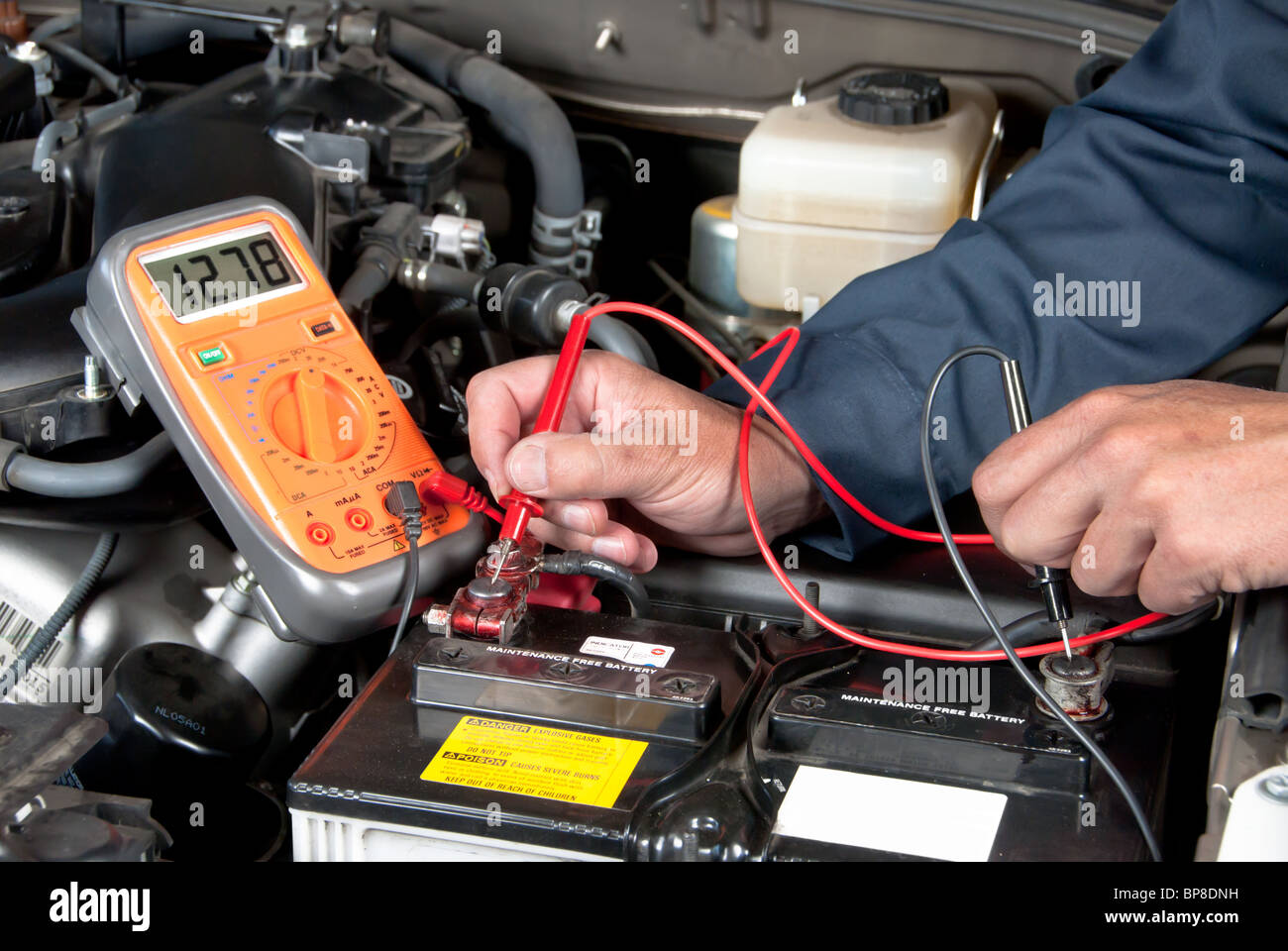 An auto mechanic uses a multimeter voltmeter to check the voltage level in a car battery. Stock Photo