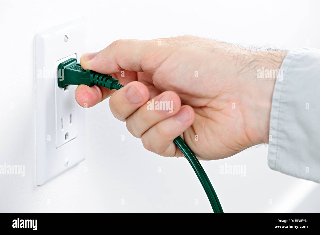 Hand pulling green electrical plug from outlet Stock Photo