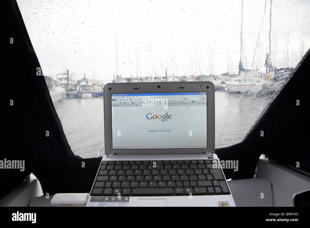 using netbook and 3g mobile internet access looking out of a boat canopy in the rain in a marina in the uk Stock Photo