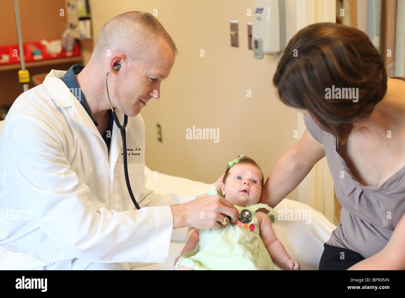 male doctor examines infant  child w/ mother in doctor's office Stock Photo