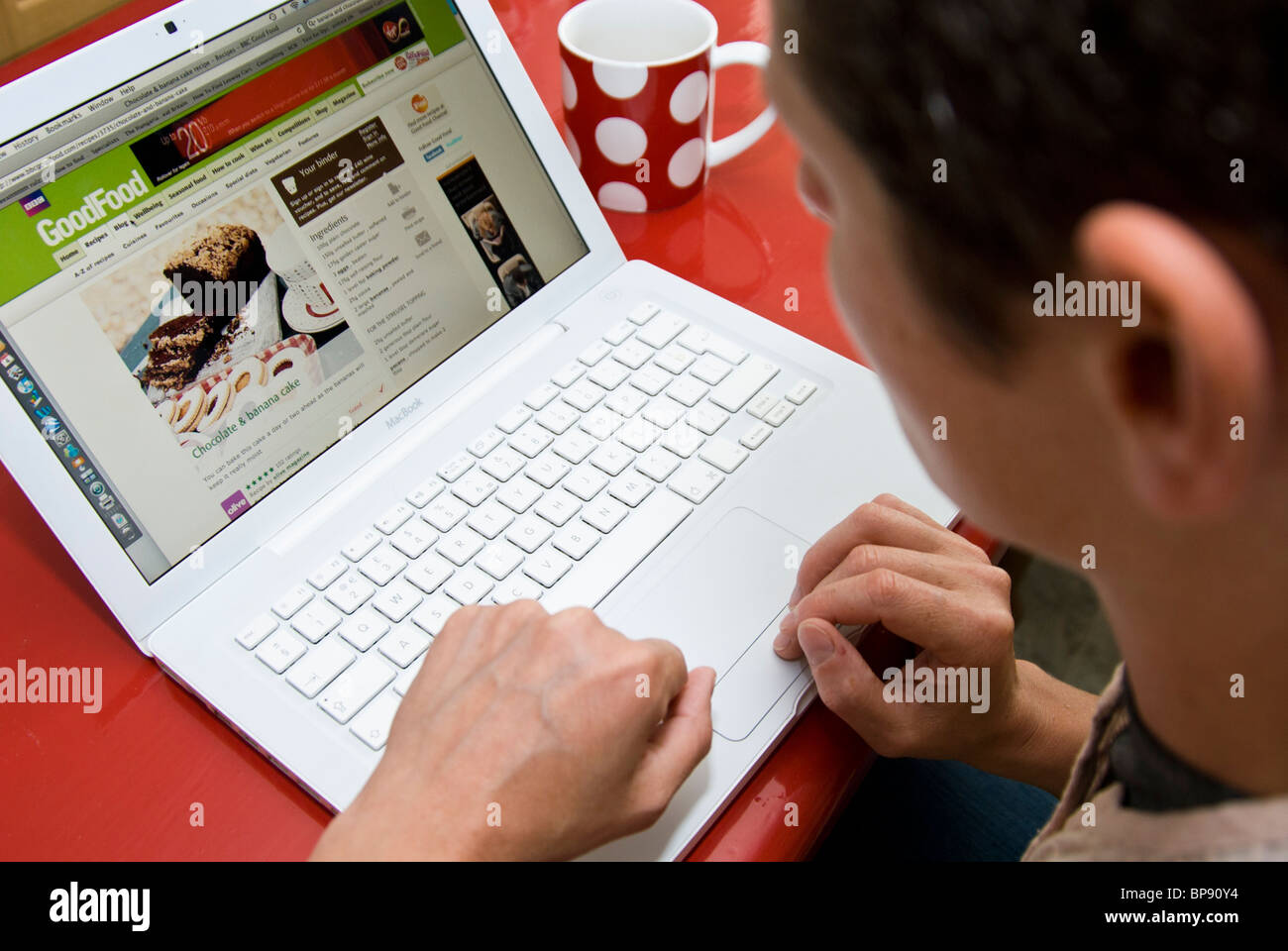 Person sat at red table searching online for recipes using a laptop ...