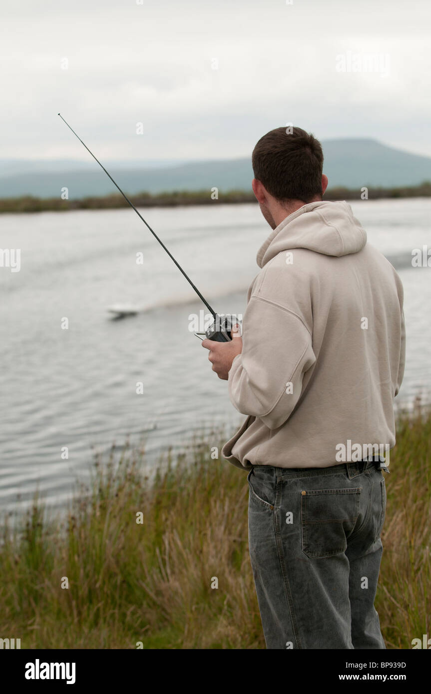 A man racing with radio - controlled model power boat on a pond, Wales UK Stock Photo