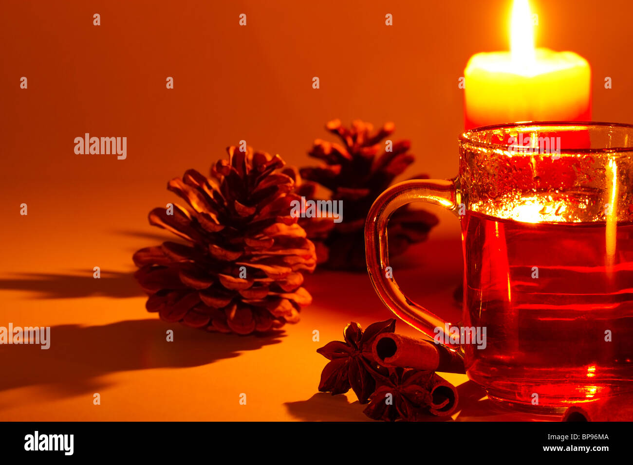 red tea in a glass, cinnamon sticks, star anise and a conifer cone at candle light Stock Photo