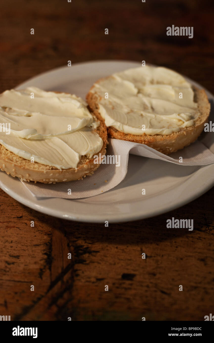 A toasted sesame bagel is served with cream cheese on a white plate. Stock Photo