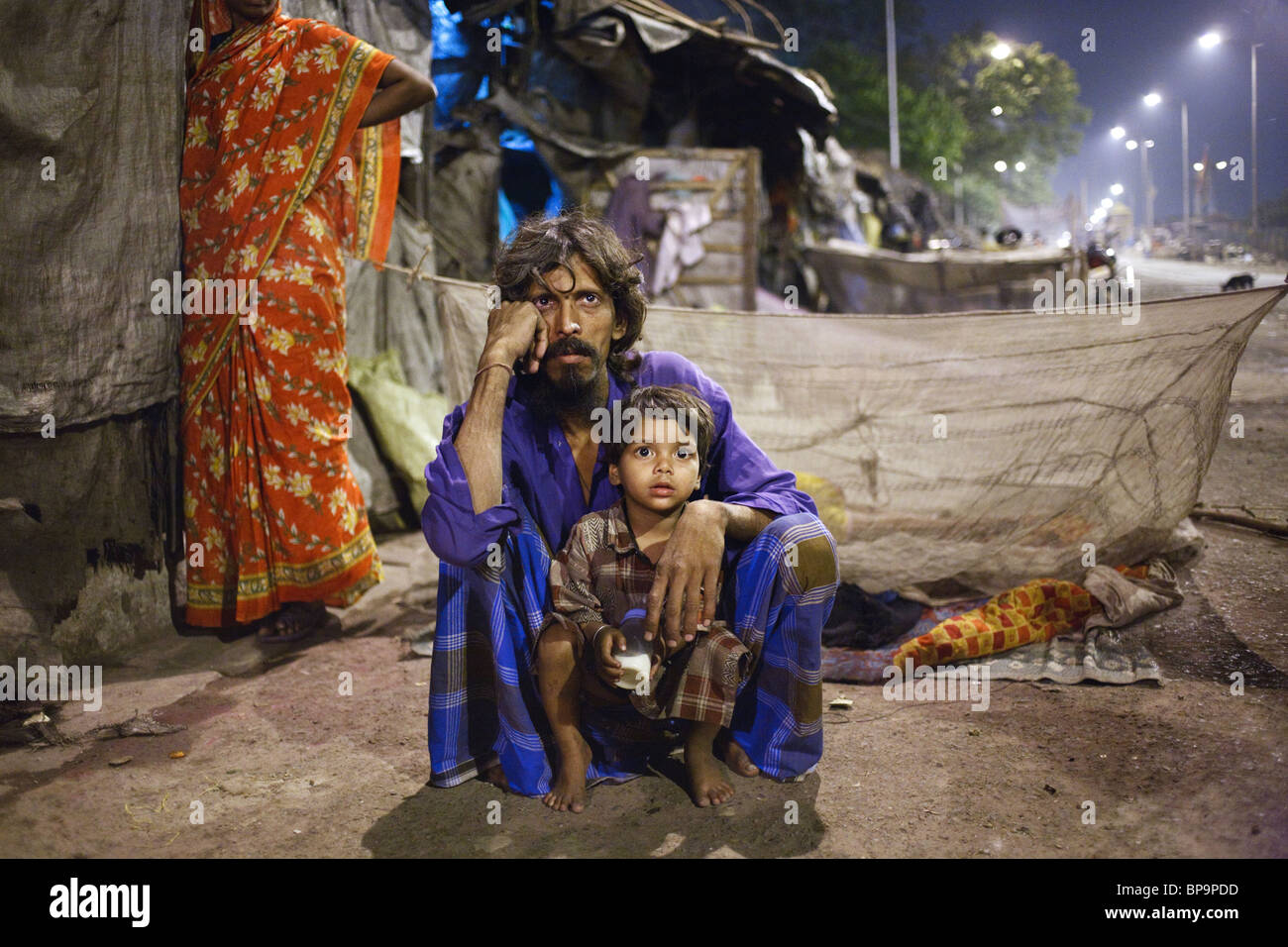 A father with his son at night outside their hut in one of the slums of Kolkata, India. Stock Photo