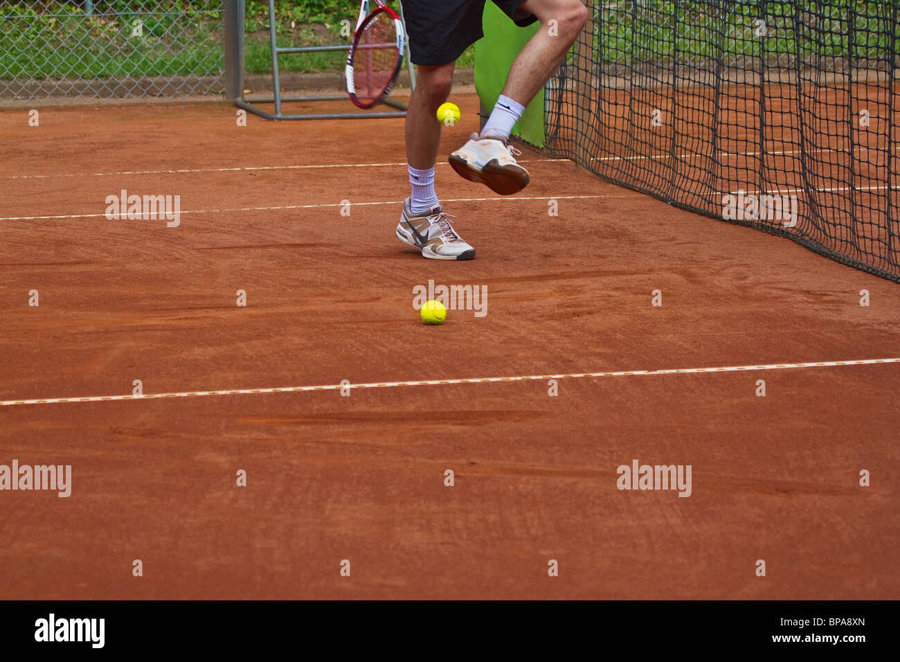 Clay court. Legs of tennis player skillful picking up the ball with his racket. Horizontal Stock Photo