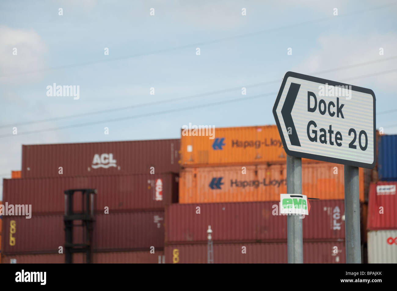 A road sign showing the words 'Dock Gate 20' with shipping containers stacked up in the A road sign showing the words 'Dock Gate 20' with shipping containers stacked up in the
