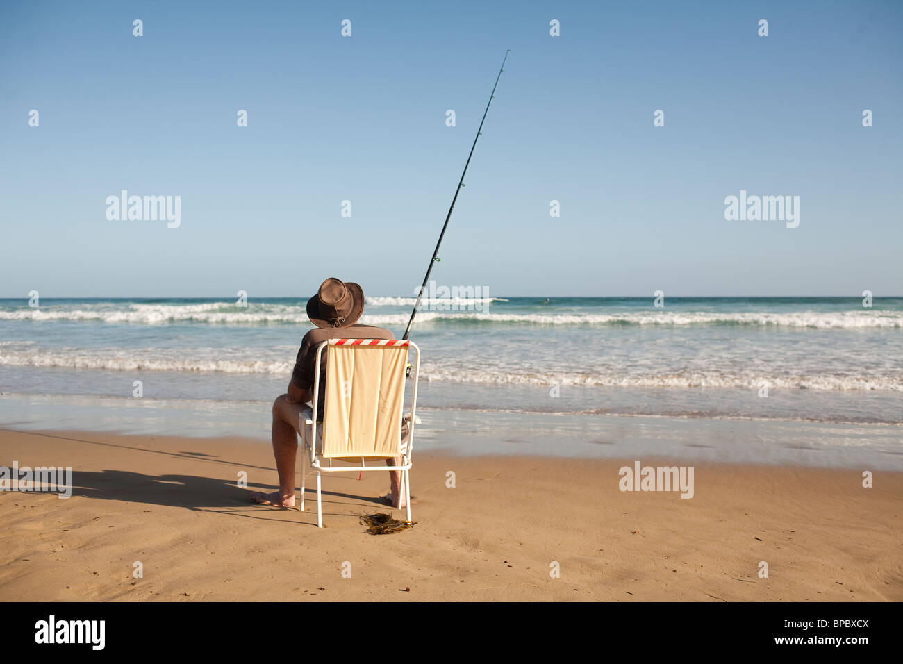Fisherman sitting in a beach chair surf casting in the ocean Stock