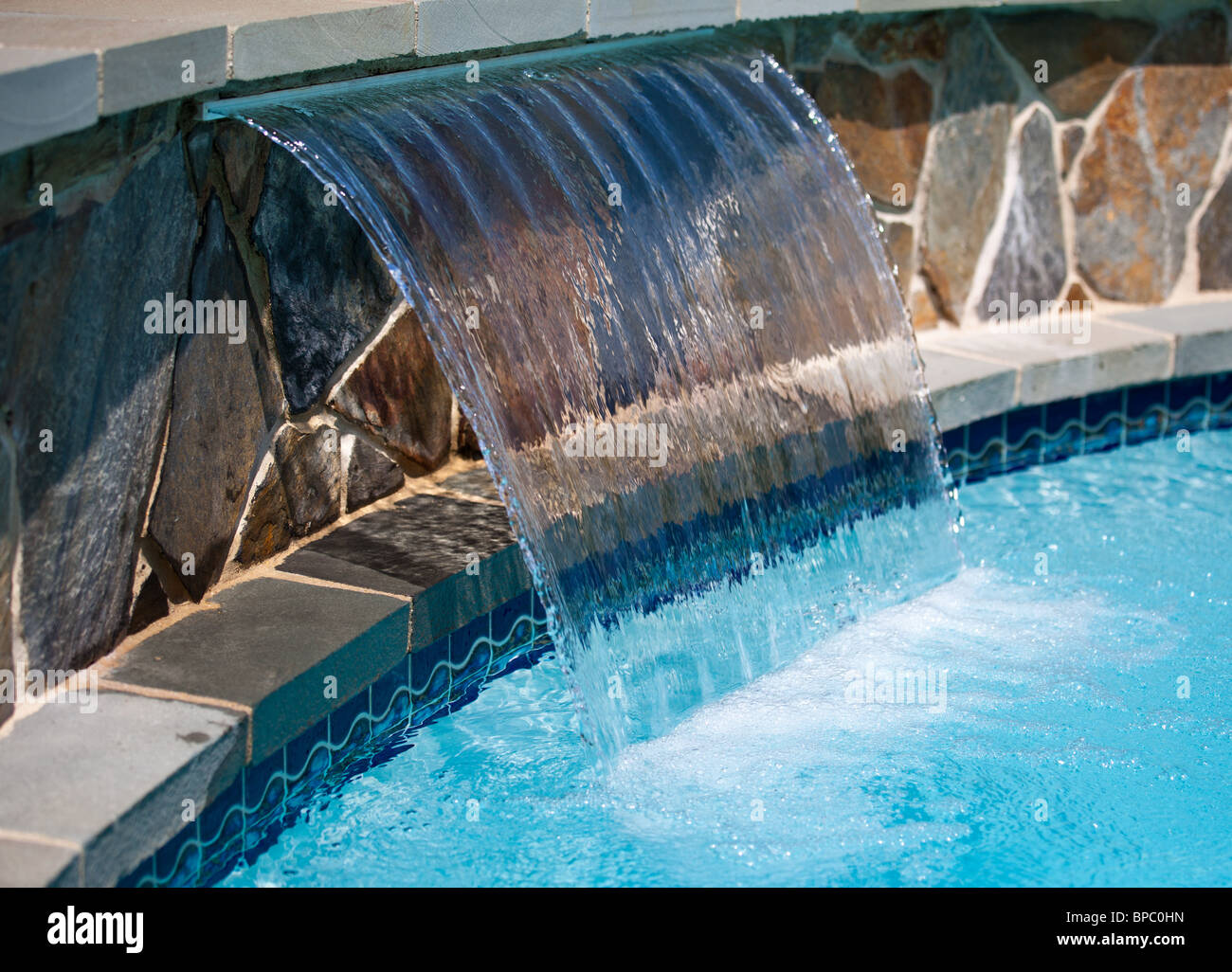 Plume of water arching out of a stone wall into a blue swimming pool ...
