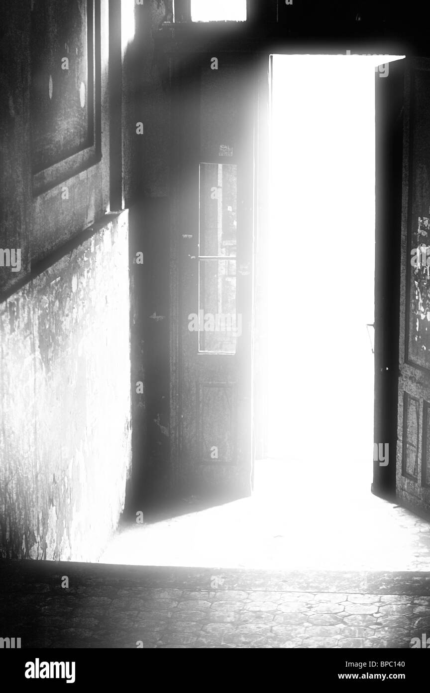 Open doorway in an old building with bright light coming out of it Conceptual artistic black-white photo Stock Photo