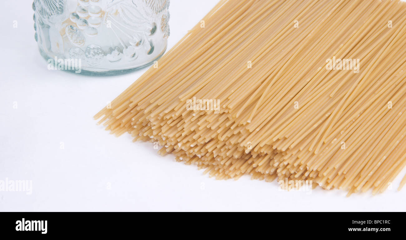 raw spaghetti noodles laying on a white background next to a glass jar. Stock Photo