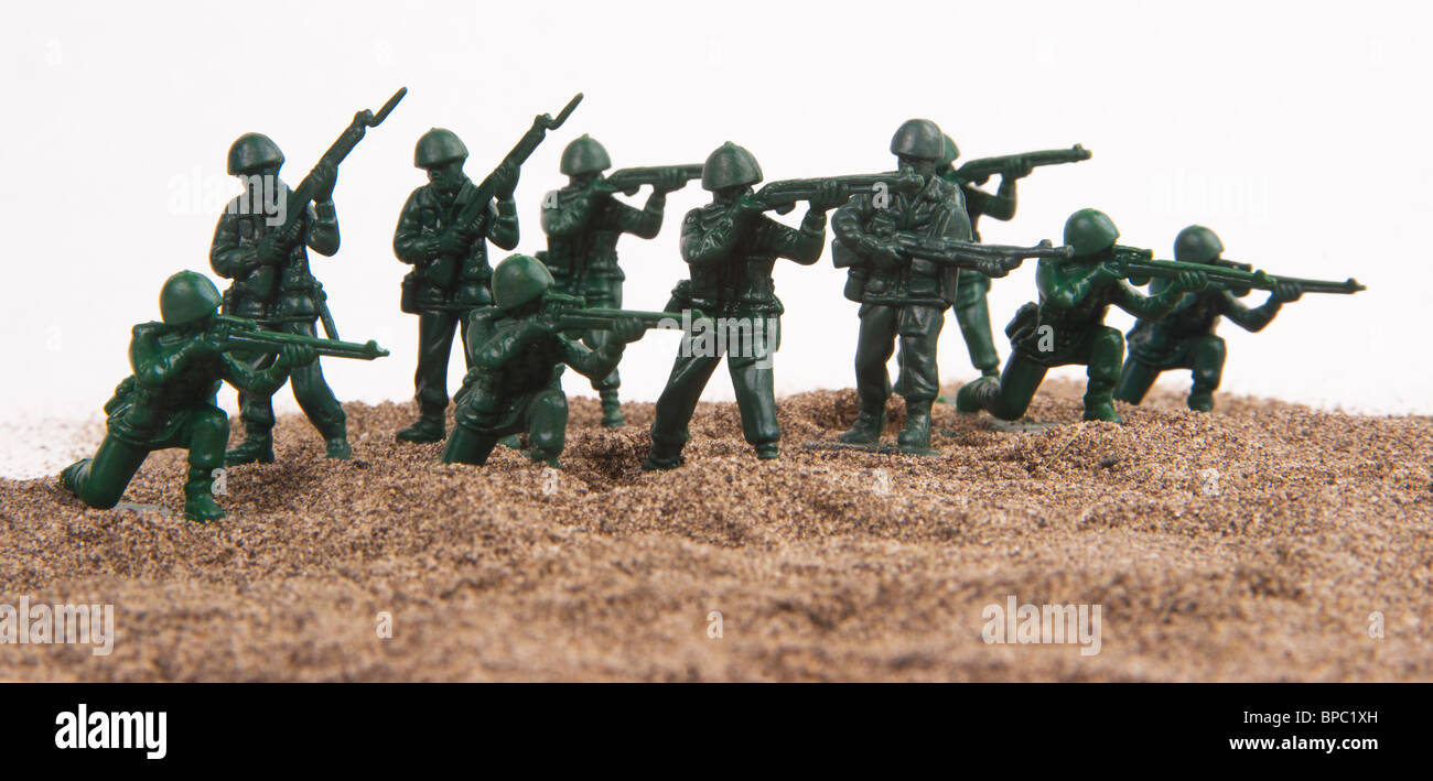 A group of little plastic green army men set up on a sandpile against a white background. Stock Photo