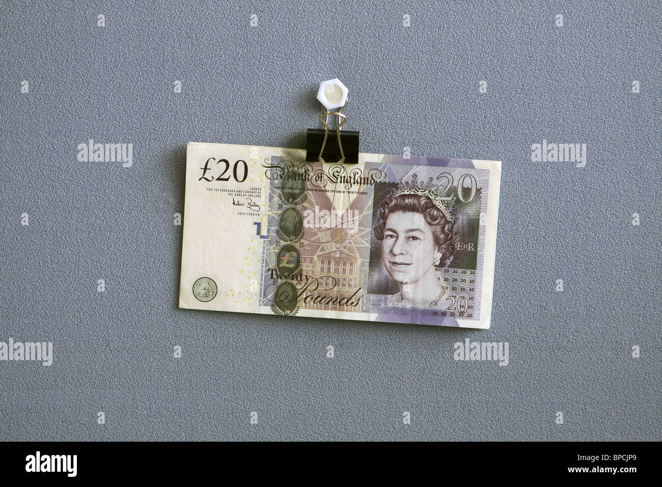 £20 note hanging from a bulldog clip against a blue cloth background Stock Photo