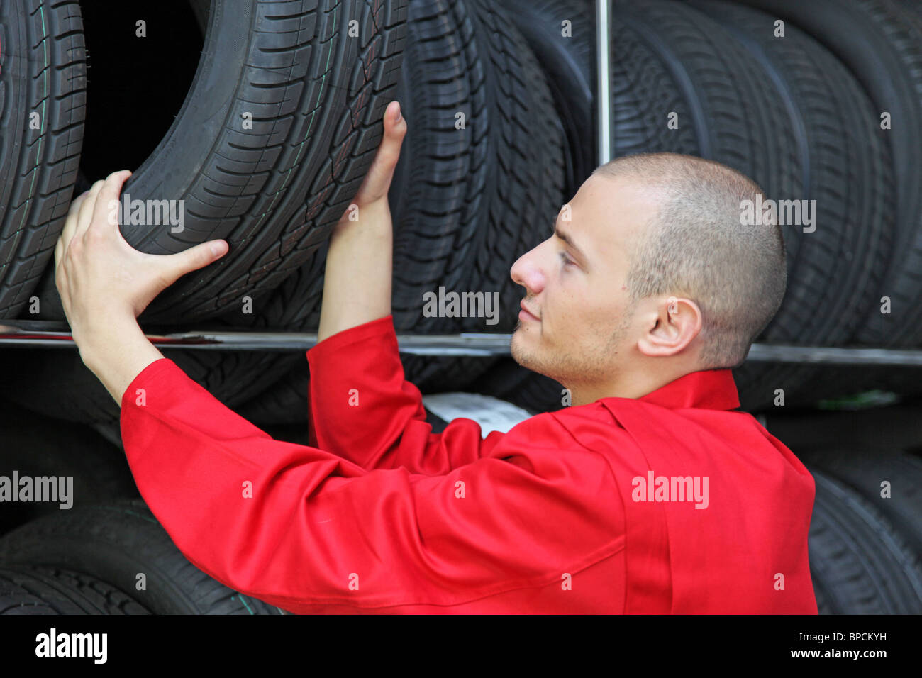 A working mechanic in a garage standing next to a rack full of tires