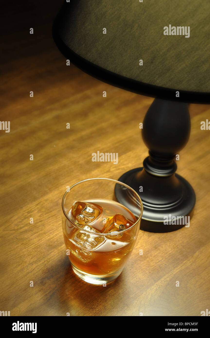 Bourbon on the rocks on wooden table illuminated by lamp. Stock Photo