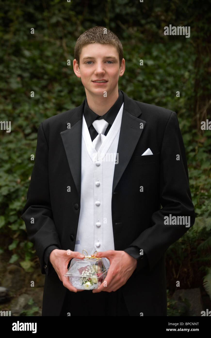 A young man in a tuxedo holds a corsage in a clear box. Stock Photo