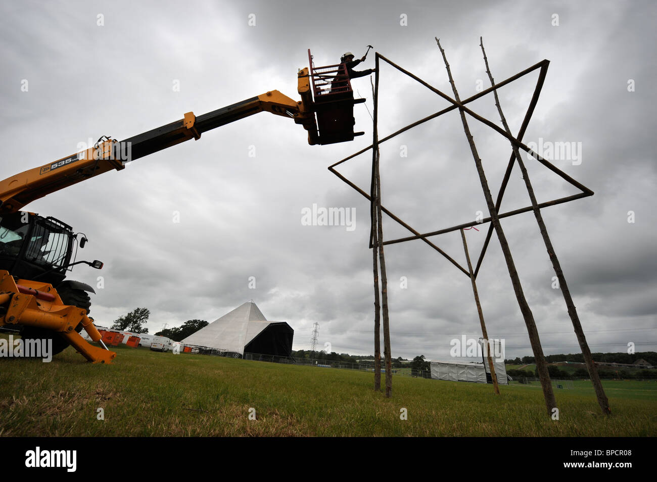 A scaffolder erects a timber star near The Pyramid Stage at the Glastonbury Festival site Pilton UK Stock Photo