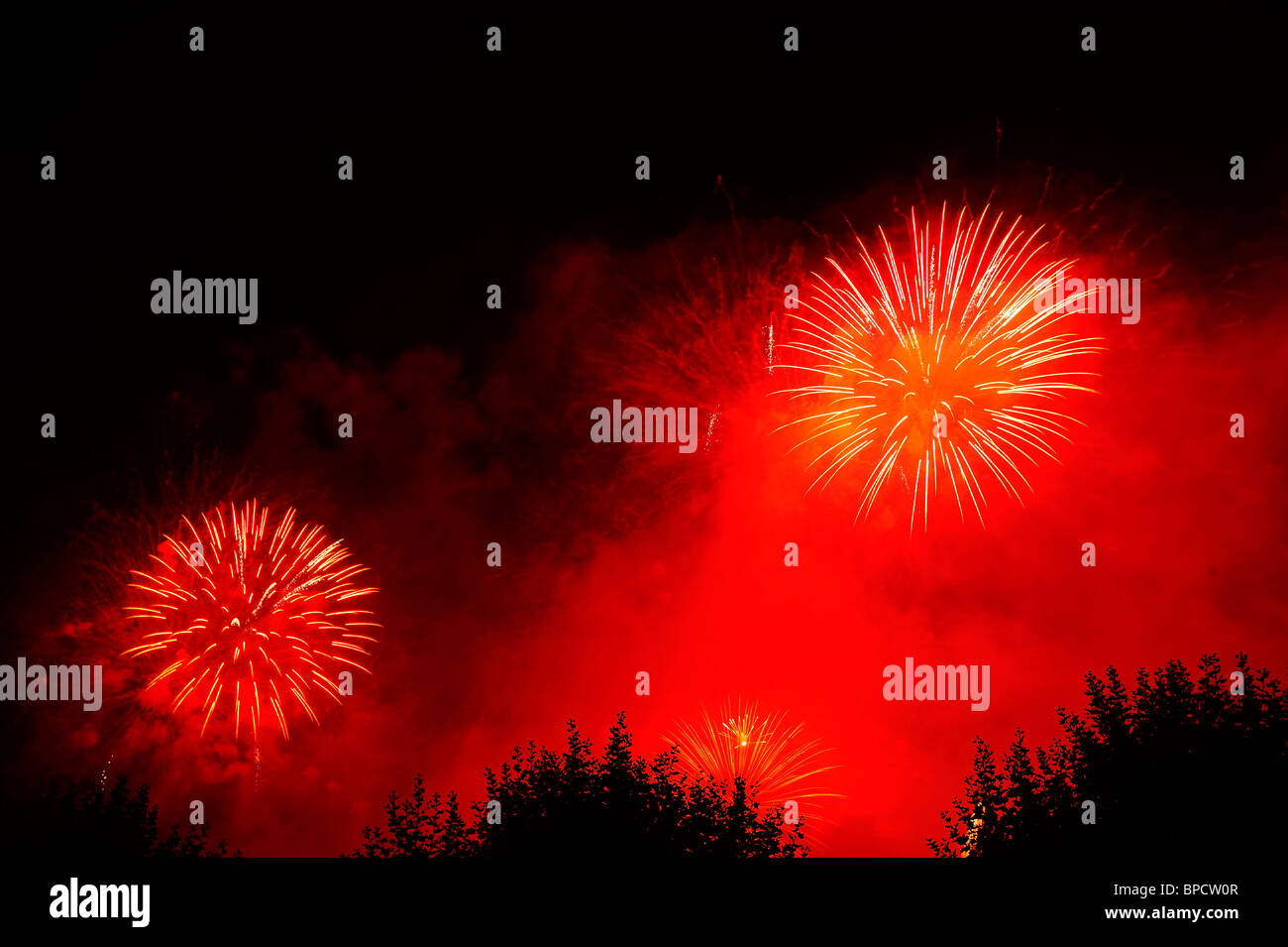 Firework bursts in the night sky against a background of red smoke. Space for text in the dark of the night sky. Stock Photo