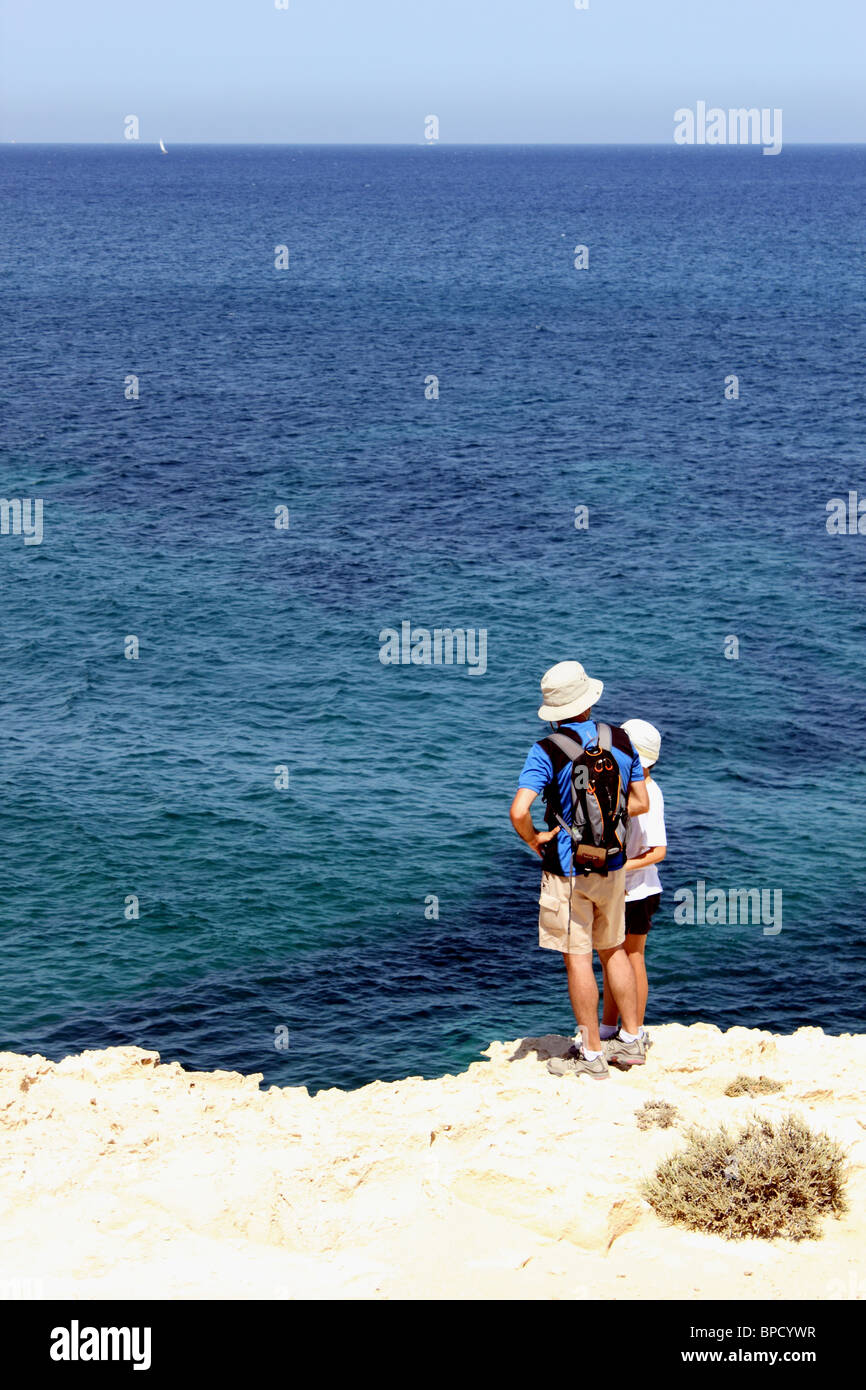 Man and boy in walking clothes with rucksack stand at cliff edge, looking to sea, El Playazo, Cabo de Gata near Las Negras Spain Stock Photo