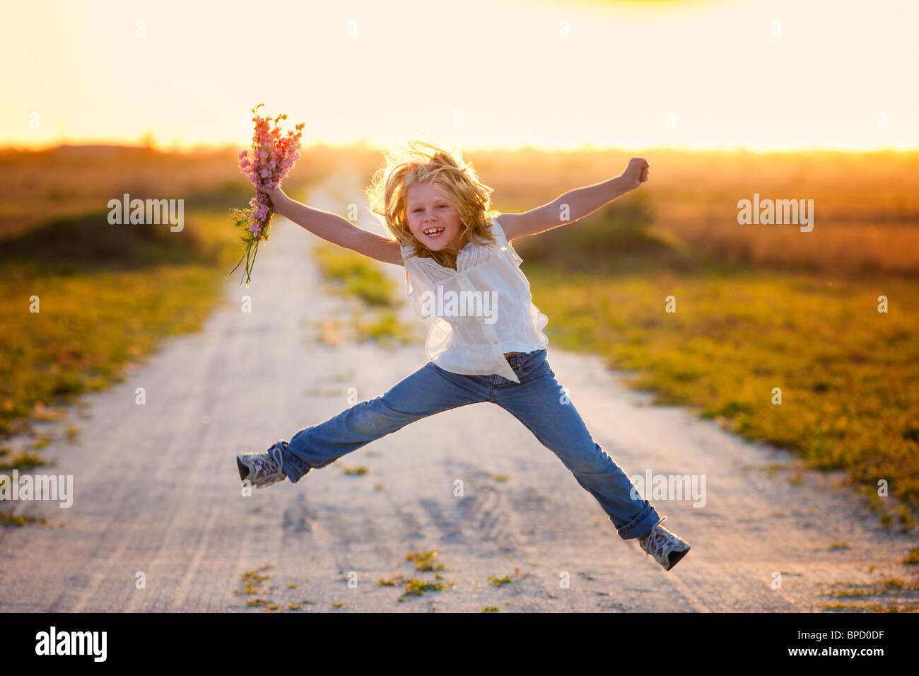 Young girl holding flowers jumping in air Stock Photo