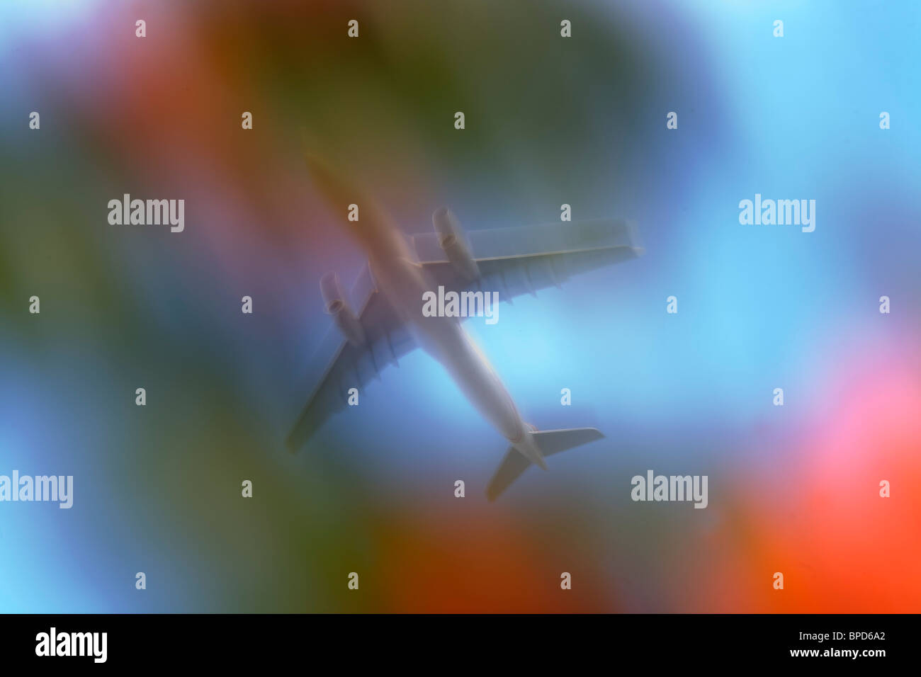 Seen through garden trees, a jet airliner passes overhead in bright skies, blurred purposely using a slow camera speed. Stock Photo